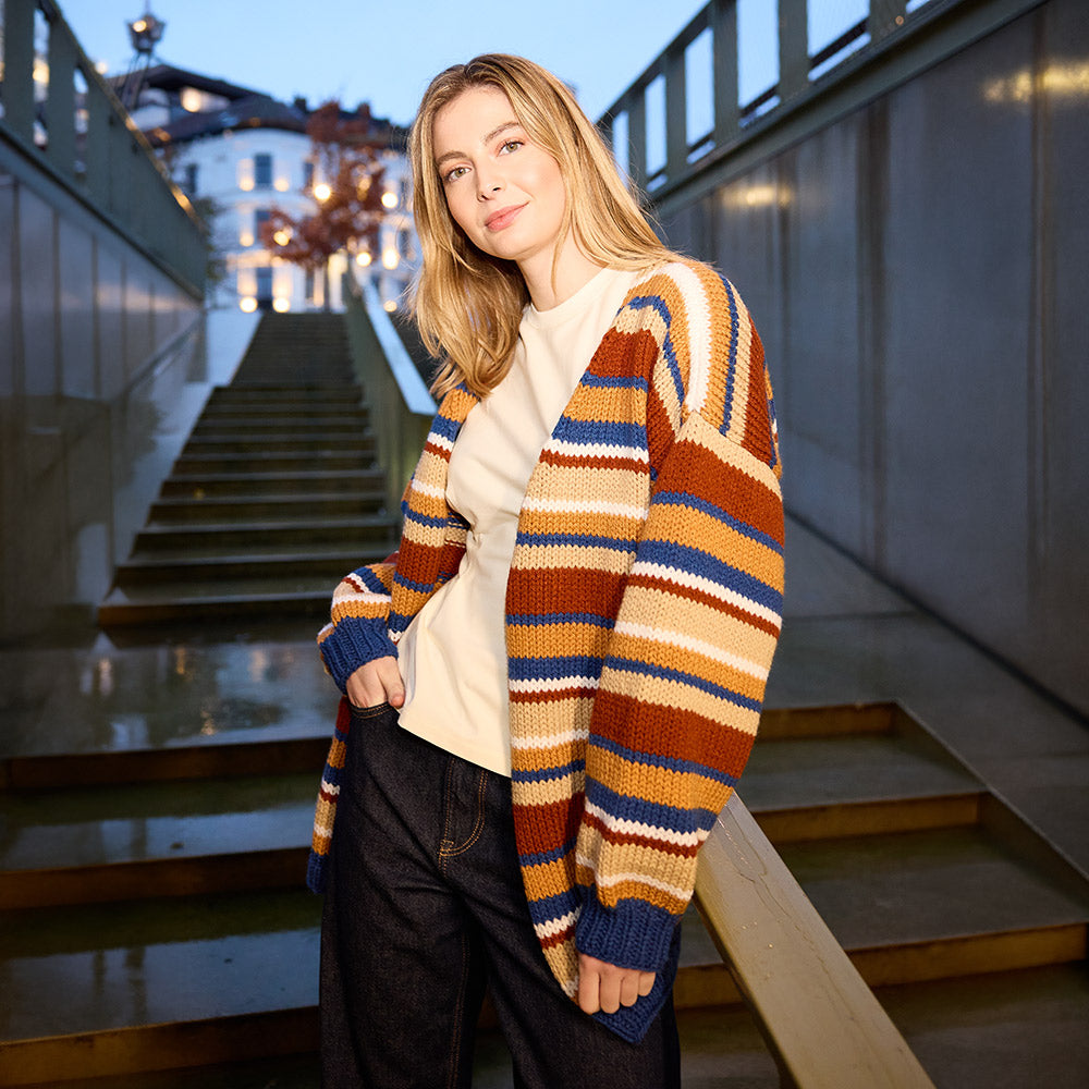 Model draagt Knipmode oversized strepenvest met blauw, oranje, bruin en wit op trap